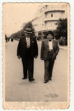 : Vintage photo shows the elegant men at the spa resort. They wear hats and slack suits. Colonnade is on background. clipart