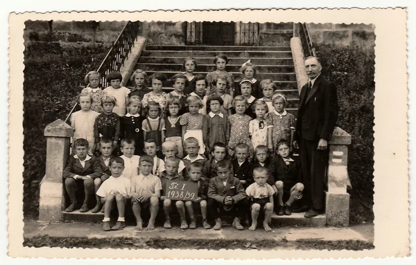 Vintage photo shows pupils (schoolmates) and their teacher pose in front of school. Black & white antique photography. — Stock Photo, Image