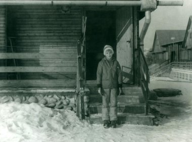 Retro photo shows a young boy in winter time. Boy stands in front of chalet with skis. Vintage black & white photography. clipart
