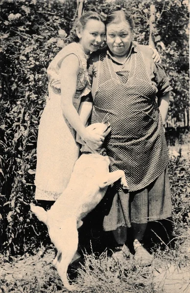 Ретро-фото показывает двух сельских женщин (мать и дочь) с собачьим ларьком в саду. Черно-белая винтажная фотография — стоковое фото
