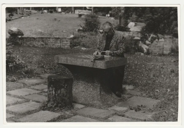 Na retro fotce je muž, který sedí u kamenného stolu venku. Černá & bílá fotografie. — Stock fotografie