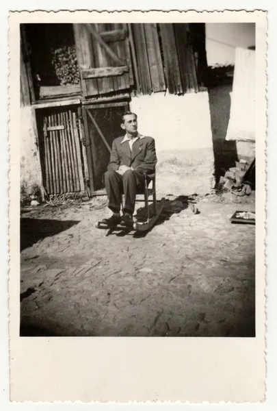 Retro photo shows a young man sits onthe rocking chair in the backyard. Vintage black & white photography. — Stock Photo, Image