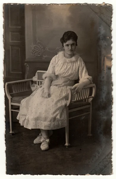 Vintage photo shows woman sits on a white period bench. Retro black & white studio photography. — Stock Photo, Image