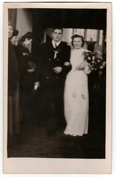 Vintage photo shows newlyweds. Wedding ceremony - bride and groom go from church/cathedral. Retro black & white photography with sepia effect. — Stock Photo, Image