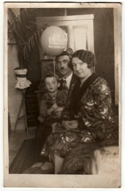 Vintage fotoğraf oturma odasında aile gösterir. Çocuk hava topu (şişme top) tutar. Retro siyah & beyaz fotoğraf.