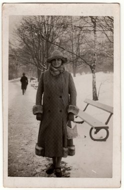 Vintage photo shows woman in a winter time. Woman wears a long coat with fur bordering.  Retro black & white photography. clipart