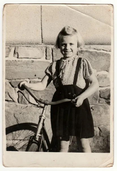 Vintage photo shows a small girl with bicycle. Retro black & white photography. — Stock Photo, Image