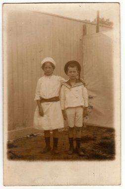 Intage fotoğraf kardeşler (kız ve erkek) arka bahçesinde poz gösterir. Erkek denizci kostümü giyer ve kız beyaz bir elbise giyer. Retro siyah & beyaz fotoğraf.