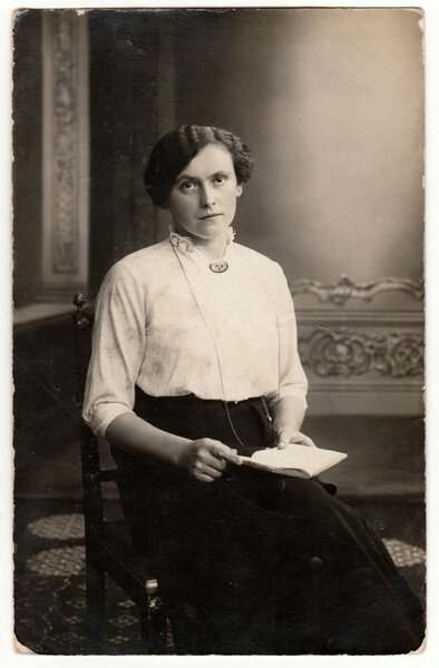 Vintage photo shows a young woman. She wears Edwardian hairstyle. Retro black & white studio photography with sepia effect.