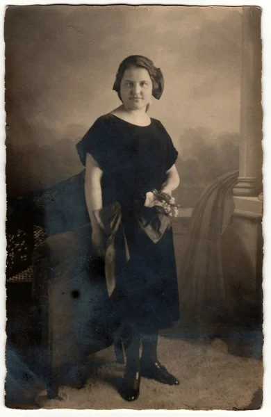Foto vintage mostra mulher com cabelo curto. Mulher usa vestido preto e segura buquê (cacho de flores). Retro preto & fotografia estúdio branco com efeito sépia . — Fotografia de Stock