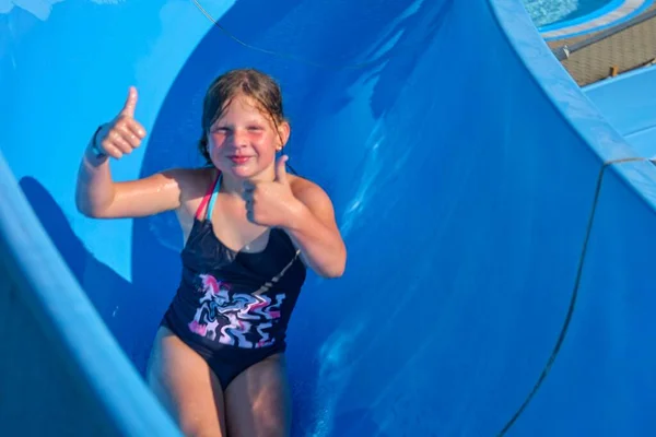 Linda niña deslizándose en el tobogán de agua. Atracción divertida de los niños en el parque acuático. Concepto de vacaciones —  Fotos de Stock