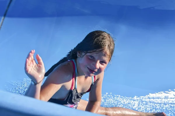 Bella bambina che scivola sullo scivolo d'acqua. Divertente attrazione per bambini al parco acquatico. Concetto di vacanza — Foto Stock