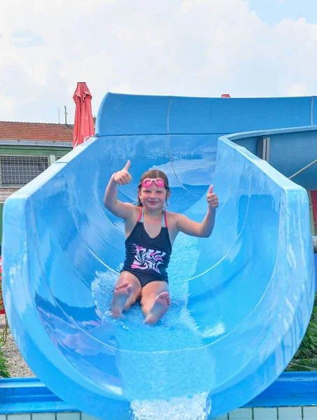 Chica deslizándose hacia abajo en un tobogán de agua en la piscina en el parque acuático. Concepto de vacaciones. Diversión festiva —  Fotos de Stock