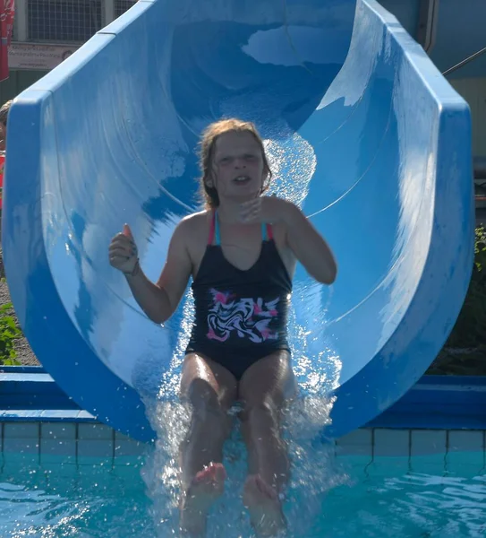 Una niña se está deslizando hacia abajo en un canal en la piscina en el parque acuático. Atracción divertida de los niños en el parque acuático. Concepto de vacaciones — Foto de Stock