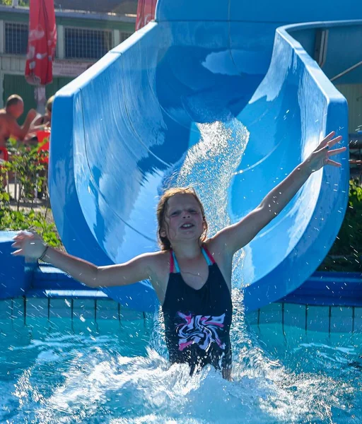 Το όμορφο κοριτσάκι γλιστράει στο νερό και γλιστράει στην πισίνα. Αστεία παιδική έλξη στο υδάτινο πάρκο. Έννοια διακοπών — Φωτογραφία Αρχείου