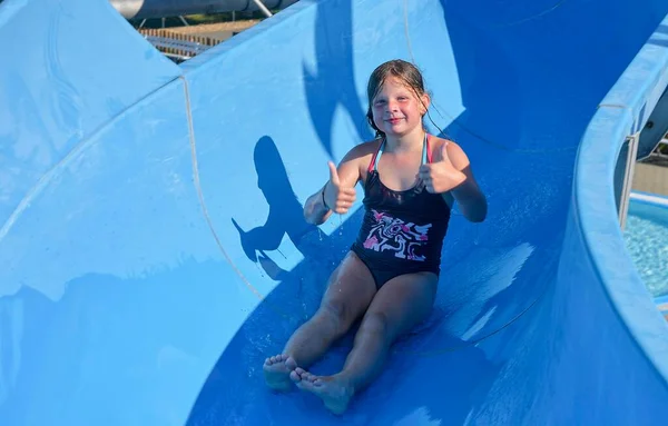 Una niña se está deslizando por un canal en el parque acuático. Atracción divertida de los niños en el parque acuático. Concepto de vacaciones —  Fotos de Stock