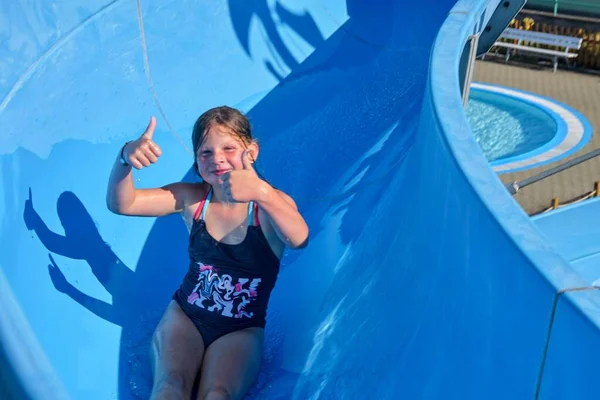 En liten flicka glider ner på en flöjt i vattenparken. Roliga barn attraktion på äventyrsbadet. Begreppet semester — Stockfoto