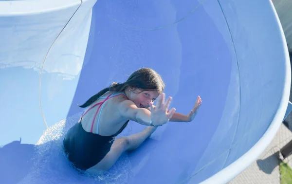 Rapaz feliz no escorrega de água no parque aquático. Corrediça de água com água salpicada fluindo no parque aquático. Férias no parque aquático de verão. Conceito de férias — Fotografia de Stock