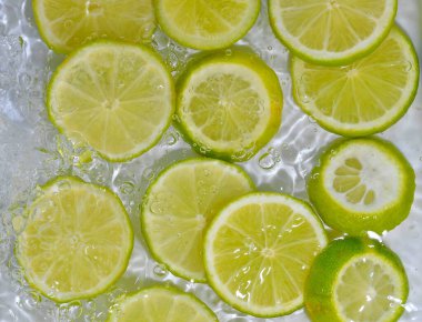 Beyaz arka planda limonlu meyve dilimleri. Limonlar kabarcıklarla sıvıya yakın çekim yapıyor. Suyun içinde sarı limon dilimleri. Sudaki meyvelerin makro görüntüsü