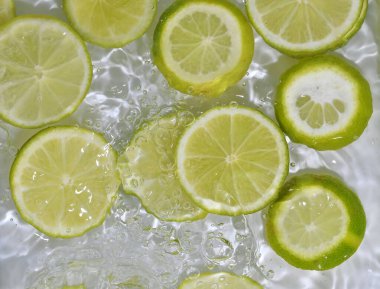Beyaz arka planda limonlu meyve dilimleri. Limonlar kabarcıklarla sıvıya yakın çekim yapıyor. Suyun içinde sarı limon dilimleri. Sudaki meyvelerin makro görüntüsü. Boşluğu kopyala