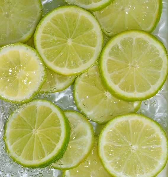 Potongan buah limau di air pada latar belakang putih. Limes close-up dalam cairan dengan gelembung. Potongan jeruk nipis kuning matang dalam air. Citra makro buah dalam air — Stok Foto
