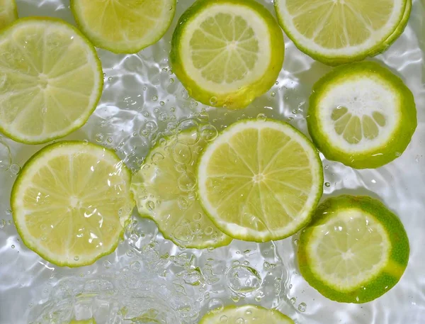 Potongan buah limau di air pada latar belakang putih. Limes close-up dalam cairan dengan gelembung. Potongan jeruk nipis kuning matang dalam air. Citra makro buah-buahan dalam air. Salin ruang — Stok Foto