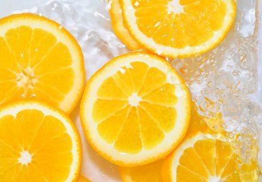 Beyaz arka planda su içinde portakal dilimleri. Portakallar kabarcıklarla sıvıya yakın çekim yapıyorlar. Suyun içinde sulu olgun portakal dilimleri. Sudaki meyvelerin makro görüntüsü