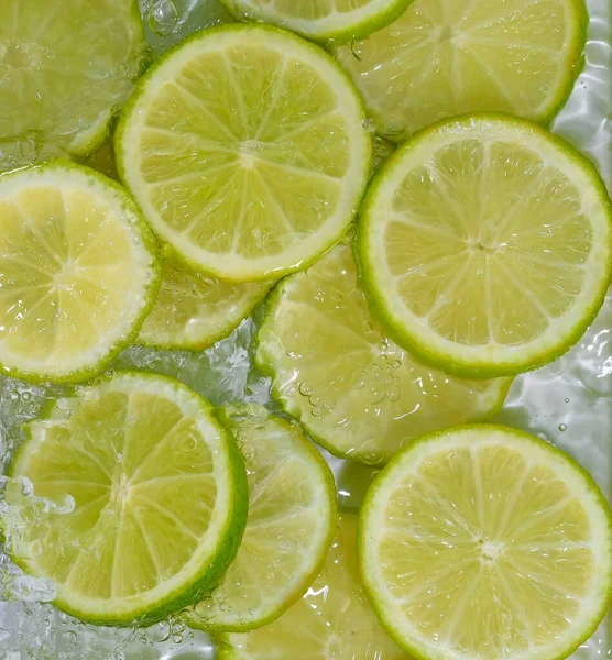 Limes close-up in liquid with bubbles. Slices of green ripe limes in water. Close-up fresh slices of yellow limes on white background