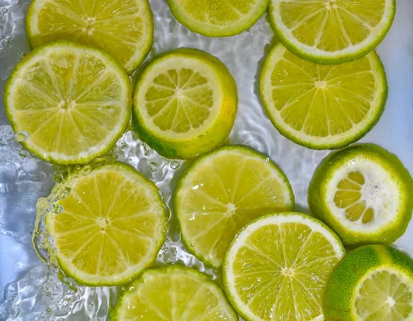 Limes close-up dalam cairan dengan gelembung. Potongan jeruk nipis hijau matang dalam air. Close-up irisan segar limes kuning pada latar belakang putih — Stok Foto