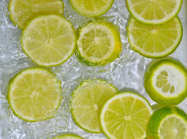 Limes close-up dalam cairan dengan gelembung. Potongan jeruk nipis hijau matang dalam air. Close-up irisan segar limes kuning pada latar belakang putih — Stok Foto