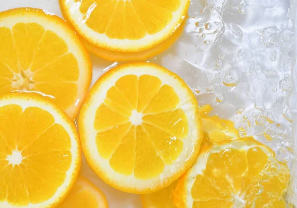 Kawałki pomarańczy w wodzie na białym tle. Pomarańcze z bliska w płynie z bąbelkami. Kawałki soczystych dojrzałych pomarańczy w wodzie. Makroobraz owoców w wodzie — Zdjęcie stockowe