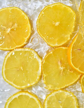 Beyaz arka planda suya limon dilimleri. Baloncuklu limonla yakından çek. Suda sarı olgun limon dilimleri. Sudaki meyvelerin makro görüntüsü