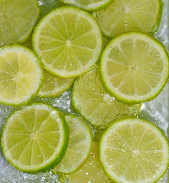 Tutup irisan segar limau hijau pada latar belakang putih. Potongan limau dalam air berkilau pada latar belakang putih, closeup. Citrus soda — Stok Foto