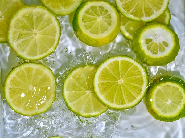 Tutup irisan segar limau hijau pada latar belakang putih. Potongan limau dalam air berkilau pada latar belakang putih, closeup. Citrus soda. Salin ruang — Stok Foto