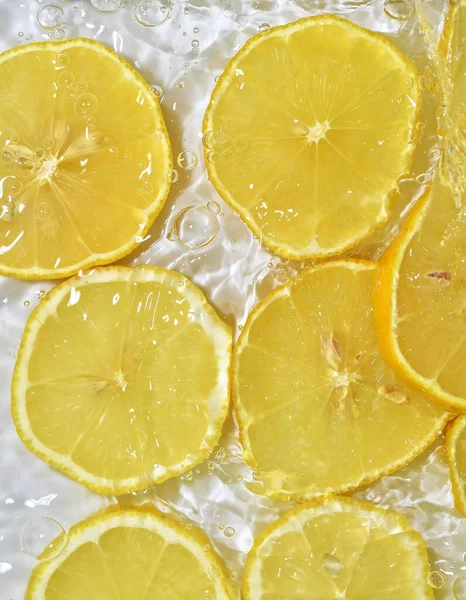 Fatias de limão na água no fundo branco. Limão close-up em líquido com bolhas. Fatias de limão amarelo maduro em água. Imagem macro de frutos na água — Fotografia de Stock