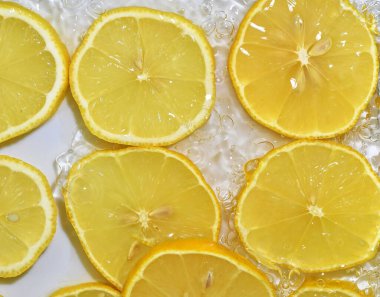 Baloncuklu limonla yakından çek. Suda sarı olgun limon dilimleri. Beyaz arka planda taze limon dilimleri.