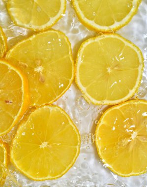 Baloncuklu limonla yakından çek. Suda sarı olgun limon dilimleri. Beyaz arka planda taze limon dilimleri.