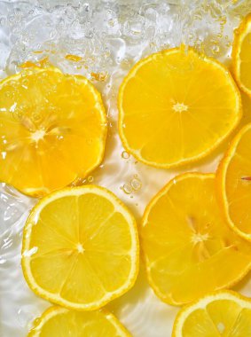 Beyaz arka planda taze sarı limon dilimleri. Beyaz arka planda köpüklü suda limon dilimleri, yakın plan. Citrus gazozu