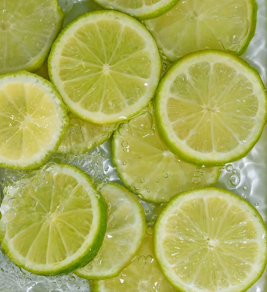 Close-up irisan segar limau pada latar belakang putih. Potongan limau dalam air berkilau pada latar belakang putih, closeup. Citrus soda — Stok Foto