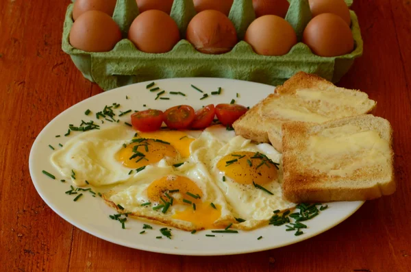 Sunny side up eggs with chives, cherry tomatoes and roasted bread with butter on red background — Stock Photo, Image