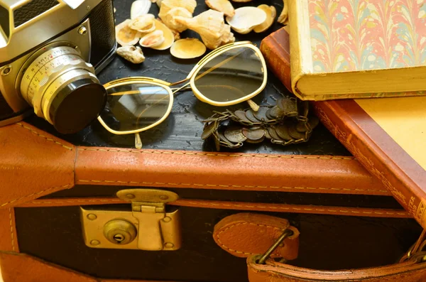 Mala vintage, câmera, óculos de sol, conchas, pulseira e uma pilha de livros. Viagem vintage . — Fotografia de Stock