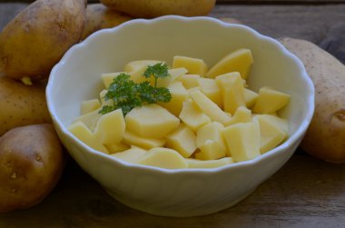 Ahşap arka plan üzerinde beyaz kase maydanoz ile soyulmuş patates