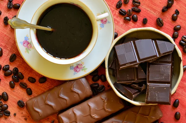 Чашка кофе с маленькими кусочками шоколада на фоне старинных чаш и кофейных зерен — стоковое фото