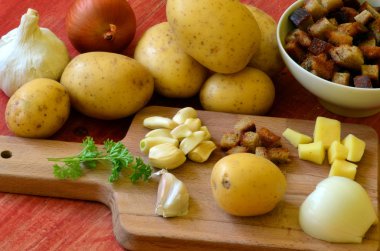 Doğrama kurulu - patates, soğan, sarımsak, kızarmış ekmek, maydanoz üzerinde sarımsak çorbası için malzemeler.