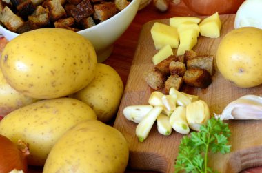 Doğrama kurulu - patates, soğan, sarımsak, kızarmış ekmek, maydanoz üzerinde sarımsak çorbası için malzemeler