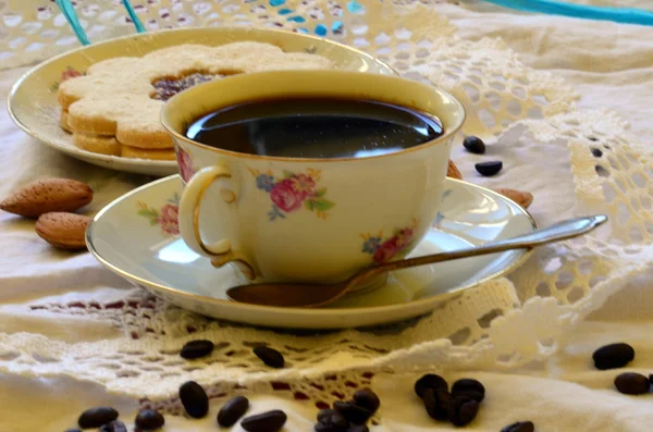 Десерты с чашкой кофе, кофейных зерен и миндаля на белой скатерти . — стоковое фото