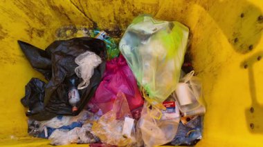 Şehirdeki bir çöp konteynırının içine bakmak. Çöp dolu sarı bir konteynır. Atık yönetimi ve çevre koruma kavramı