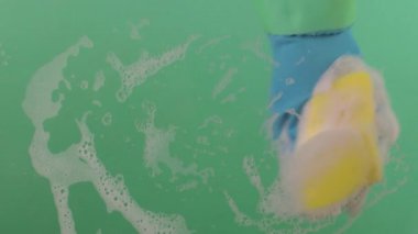 Lastik eldivenin içinde süngerle yüzeyi yıkayan bir el. Ellerin lastik eldivende olsun süngeri tut ve yüzeyi fırçala. Sünger, krom bir anahtarın üzerindeki köpüklü temizleyiciyle kaplıdır.