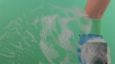 Lastik eldivenin içinde süngerle yüzeyi yıkayan bir el. Ellerin lastik eldivende olsun süngeri tut ve yüzeyi fırçala. Sünger, krom bir anahtarın üzerindeki köpüklü temizleyiciyle kaplıdır.