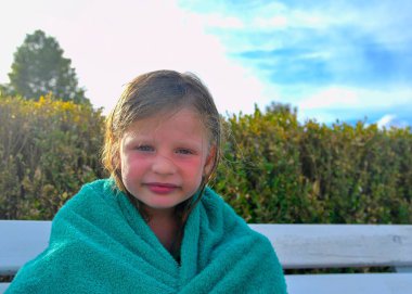 Havlu takmış gülen küçük bir kız havuzda bir bankta oturuyor. Yaz tatili konsepti, tasasız günler ve mutlu bir çocukluk.